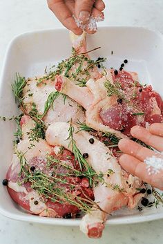 hands sprinkling seasoning onto raw fish in a white dish