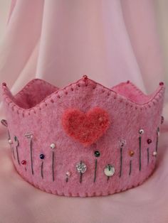 a pink felt crown with a heart on it's side and pins in the middle