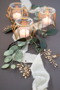 candles and greenery on a table with white napkins, eucalyptus leaves and gold candle holders