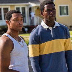 two men standing next to each other in front of a yellow and blue house on a sunny day