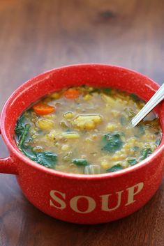 a red bowl filled with soup sitting on top of a wooden table next to a spoon