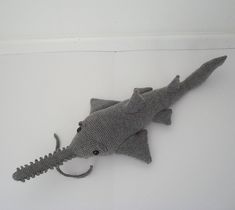 a stuffed toy shark laying on top of a white wall next to a black cat