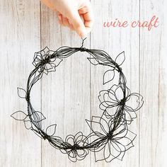 a hand holding a wire wreath on top of a white wooden table with text overlay