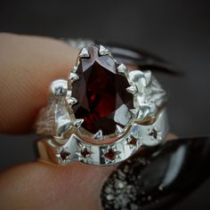 a close up of a person's hand holding a ring with a red stone