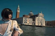 a woman standing next to a body of water in front of a large white building