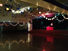 an empty room with lights and decorations hanging from the ceiling in front of a stage