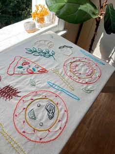 an embroidered tablecloth on a wooden table with a plant in the window sill