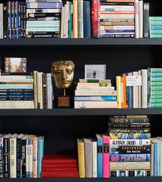 a bookshelf filled with lots of books and a golden mask on top of it