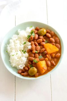 a bowl filled with beans and rice on top of a white wooden table next to a fork