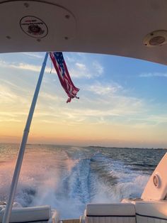 an american flag is flying from the back of a boat in the ocean at sunset