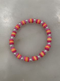 a pink and orange beaded bracelet on a white surface with silver beads in the middle