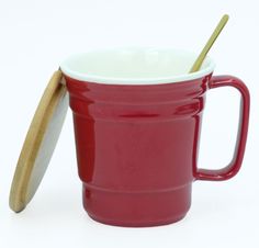 a red coffee cup with a gold lid and spoon in front of the mug is on a white surface