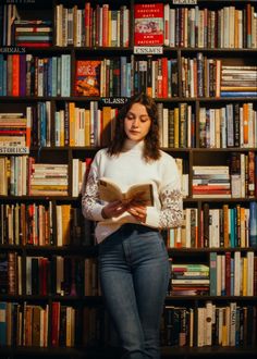 a woman standing in front of a bookshelf holding a book and looking at the camera