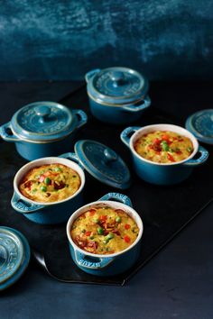 several blue pots with food in them sitting on a black tray next to each other