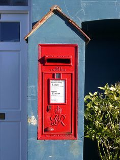 a red mailbox sitting on the side of a blue building next to a bush