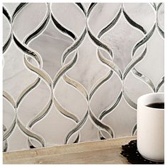 a white coffee cup sitting on top of a wooden table next to a tile wall