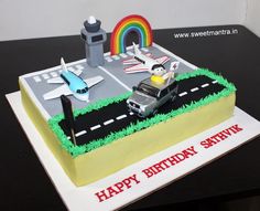 a birthday cake with an airport scene and rainbow in the background on a table top