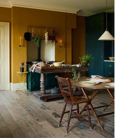 a table and chairs in a room with yellow walls, wood floors and green cabinets