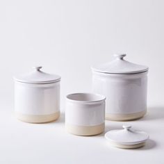 three white and beige canisters with lids sitting on a plain surface, next to each other