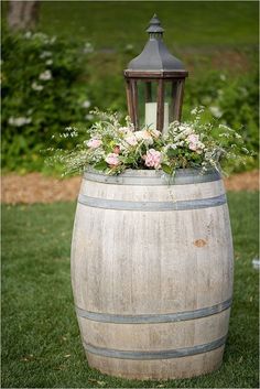 a wooden barrel with flowers and a lantern on top is sitting in the grass outside