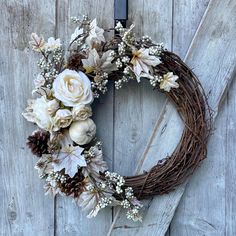 a wreath with white flowers and pine cones is hanging on a wooden door, ready to be used as a decoration