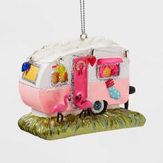 a pink and white camper ornament hanging from a tree