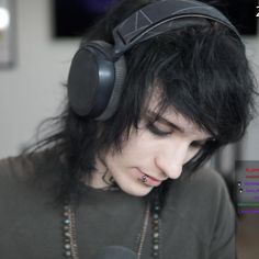 a man with black hair wearing headphones and looking at his cell phone in front of him