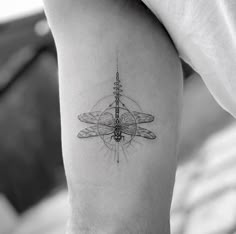 a black and white photo of a dragonfly tattoo on the right thigh, with a compass in the middle