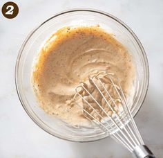 a glass bowl filled with batter and whisk on top of a white counter