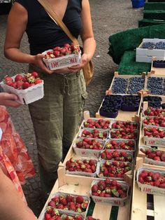 a woman is holding baskets of strawberries at an outdoor farmers market with other fruit on display