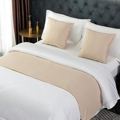 a bed with white sheets and beige pillows