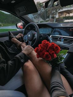 a woman sitting in the driver's seat of a car holding a bouquet of red roses