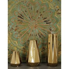 three gold vases sitting next to each other in front of a colorful wallpaper