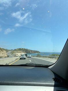 cars driving on the highway near an ocean and cliffs in the distance with blue skies