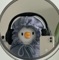 a stuffed penguin with headphones is in front of a mirror that has a cell phone on it