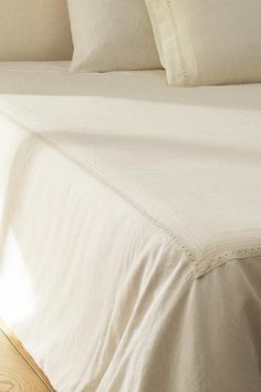 a bed with white sheets and pillows on top of it, in a room that has wood flooring