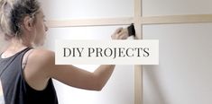 a woman is painting the wall with white paint and black brush in front of it that says diy projects