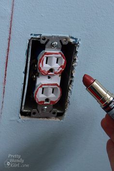 a person is holding a red lipstick in front of an electrical outlet