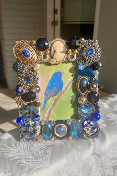 a blue bird sitting on top of a table next to a frame with beads and jewels