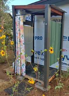 an outhouse with sunflowers in the foreground and a blue sky behind it