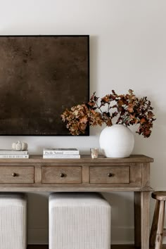 two white vases sitting on top of a wooden table next to a large painting