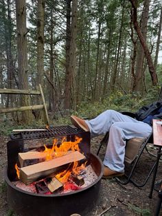 a man sitting in a chair next to an open fire pit with logs on it