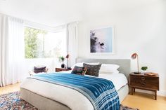 a bedroom with white walls and wooden flooring has a large bed covered in blue blankets