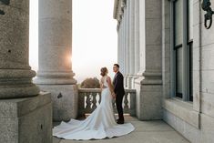 a bride and groom standing on the balcony of an old building with columns in front of them