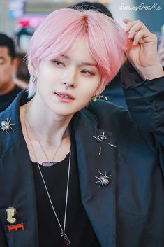 a young man with pink hair wearing a black jacket and spider pendants on his ear