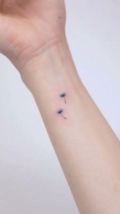 a small tattoo on the wrist of a woman's left arm, with three blue dandelions