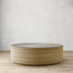 a round wooden table with glass top on a hard wood floor in front of a white wall