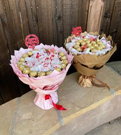 two bouquets of flowers with chocolates in them on a stone slab next to a wooden fence