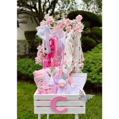 a pink and white baby's gift box with clothes in it on a stand