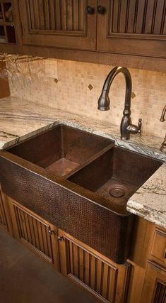 an image of a double sink in a kitchen with marble counter tops and wooden cabinets